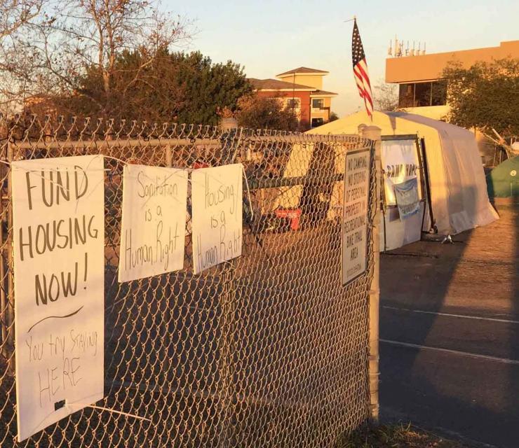 Protest signs hung by a homeless encampment in Orange County. The second sign from the left declares "sanitation is a human right." 
