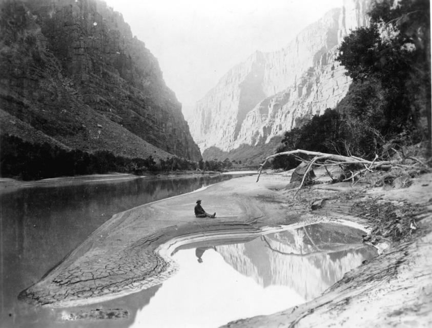 A member of Powell's second Colorado River expedition, seated and reflected in the Green River, 1871. 