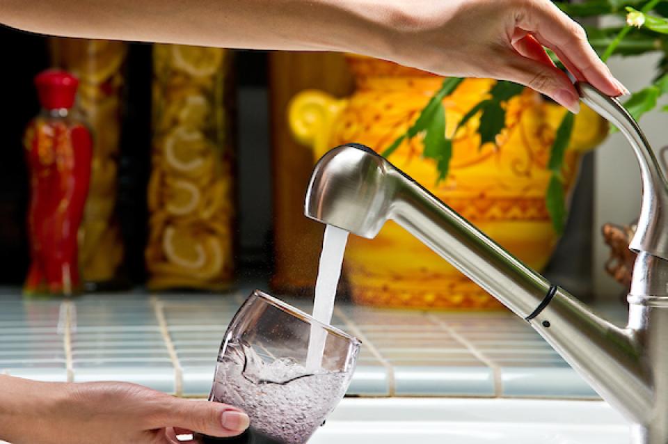 Photo of drinking water filling a glass over the kitchen sink. 