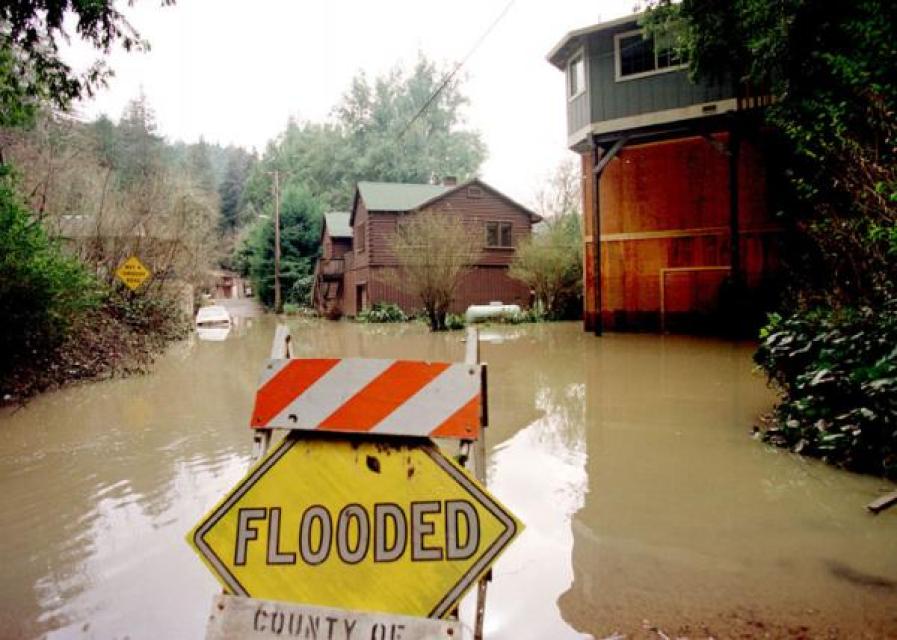 Image shows a flooded roadway near homes.