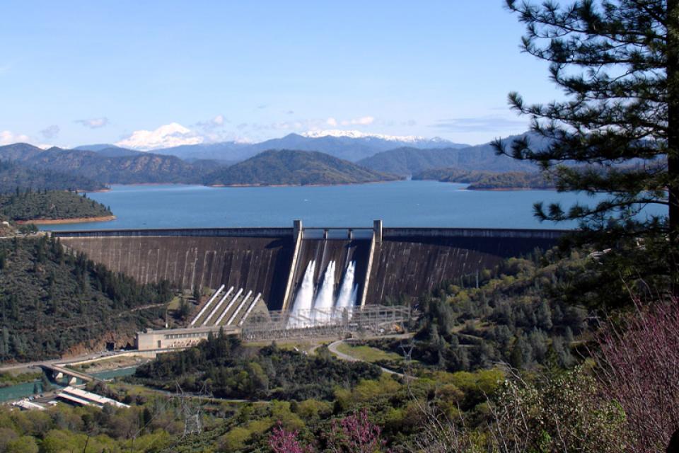 Image shows Shasta Dam from a distance, with the reservoir largely filled.